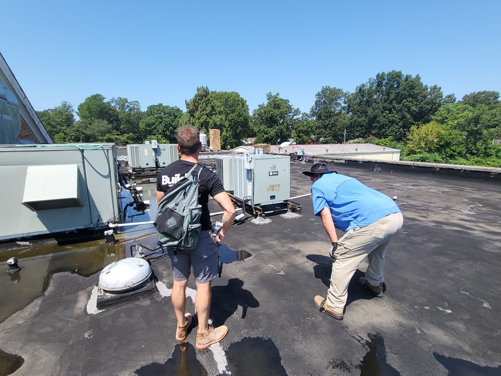Two crew members inspecting a commercial flat roof beside rooftop HVAC units