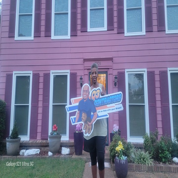 Homeowner holding the contractor yard sign in front of their two-story home after roof work