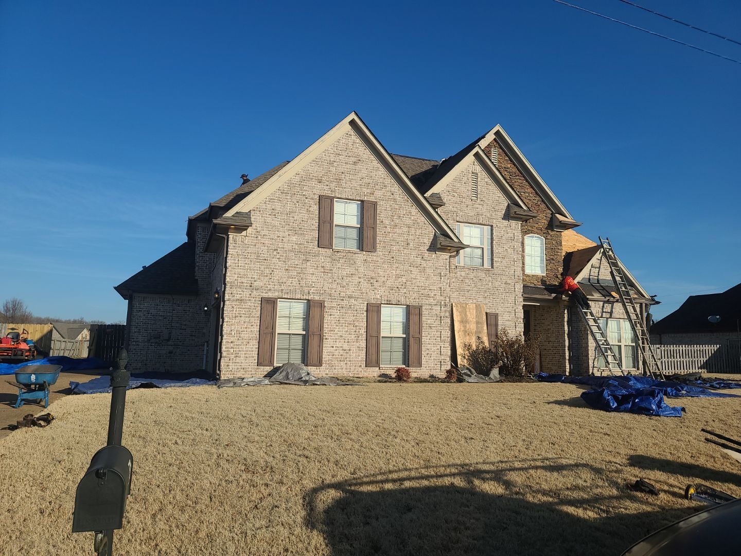 Roofing crew working on a two-story brick home during a full roof replacement, with tarps protecting the yard
